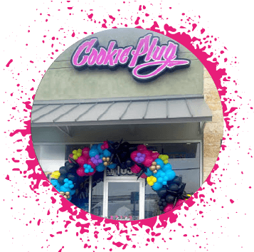 Light green storefront with a pink, white, and black sign that says 'Cookie Plug' with balloons around the door for a Grand Opening.